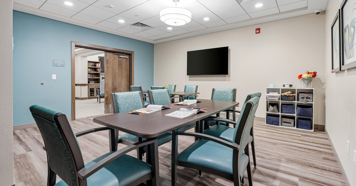 Memory care activity room at Meadowview of Johnston with table, chairs, coloring materials and a TV for resident programming