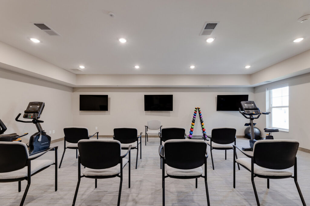 Exercise room at Meadowview of Johnston featuring stationary fitness equipment, free weights, and seating for group wellness activities.