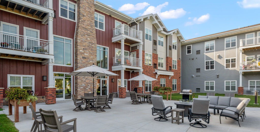 Outdoor courtyard patio at Meadowview of Johnston senior living community featuring resident seating, dining tables, and apartment balconies.