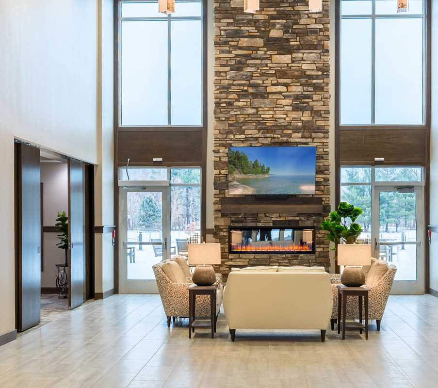 Stone fireplace and comfortable seating area in the Meadowview of Johnston lobby with large windows overlooking the courtyard.