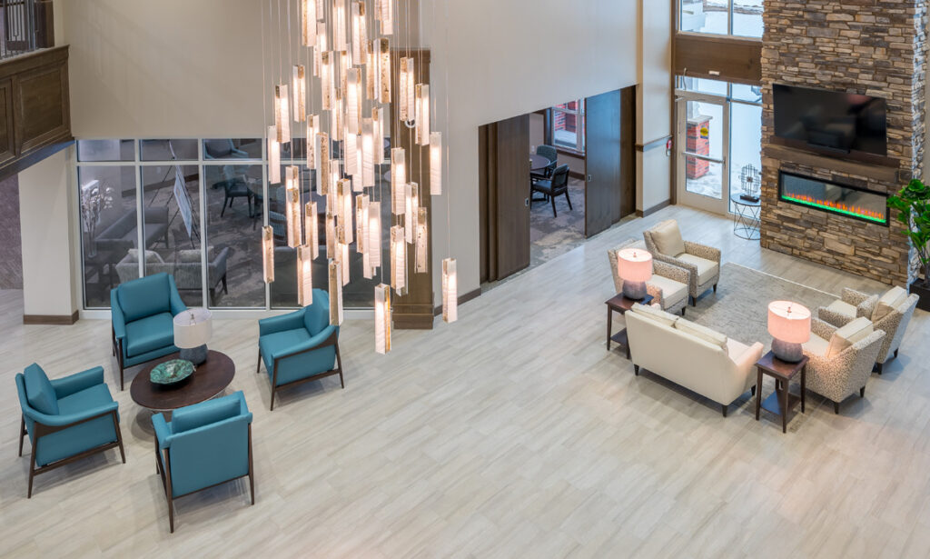 Lobby seating area at Meadowview of Johnston featuring a stone fireplace, comfortable gathering spaces, and views of the courtyard.