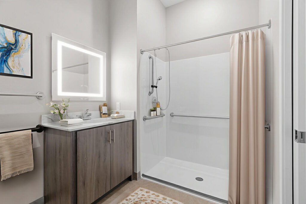 Accessible memory care bathroom at Meadowview of Johnston featuring a walk-in shower, grab bars, vanity storage, and safety-focused design for residents with memory loss.