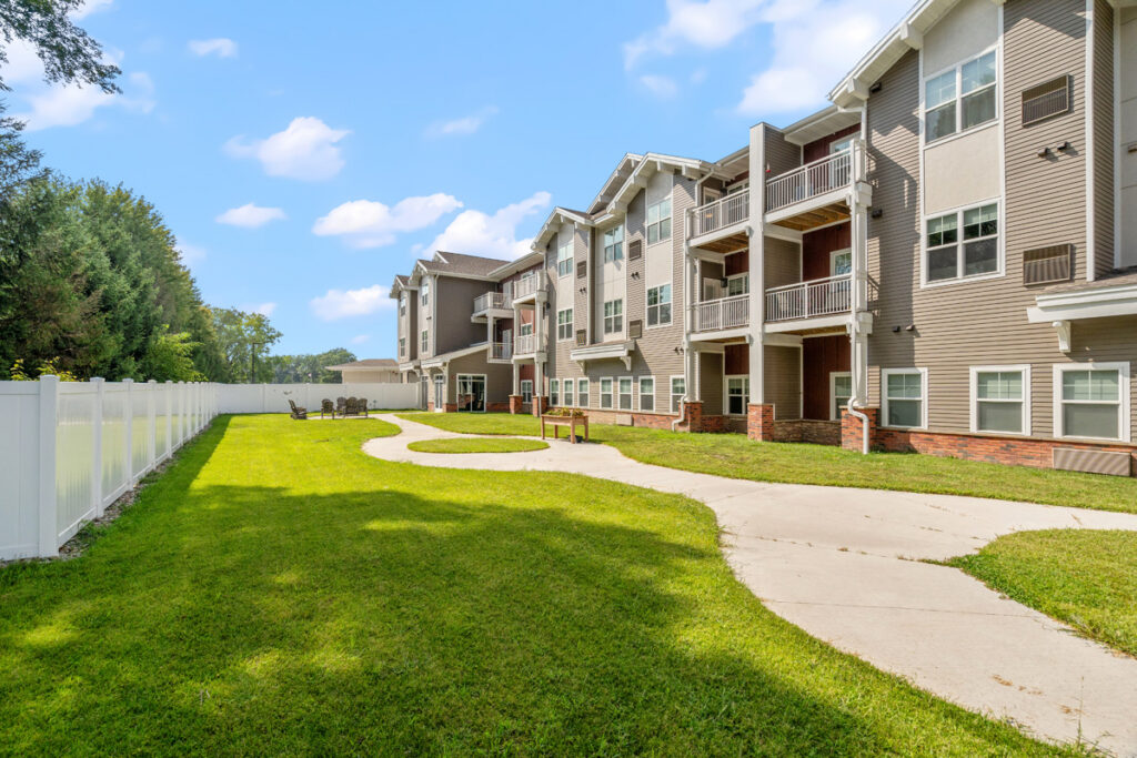 Secure outdoor memory care courtyard at Meadowview of Johnston featuring walking paths, landscaped green space, and access to resident suites and common areas.